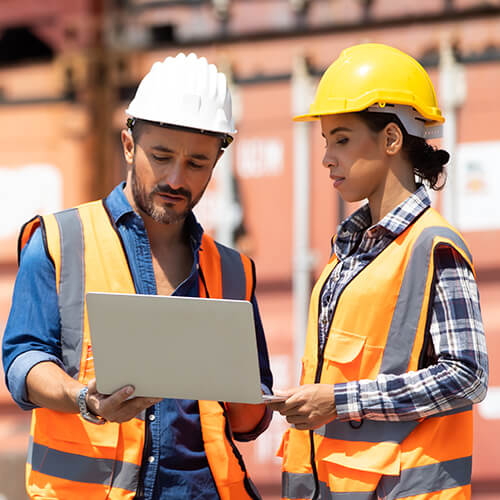 Two workers with a laptop in front of cargo containers